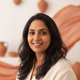 Smiling South Asian woman in her 30s, headshot portrait, soft-focus background.